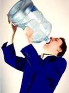 A man holding up a 5 gallon jug filled with water and pouring the water into his mouth. 