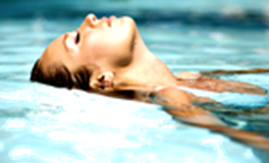 Profile of a woman resting her head at the edge of pool as she is lying in a pool of clear sparkling structured water.